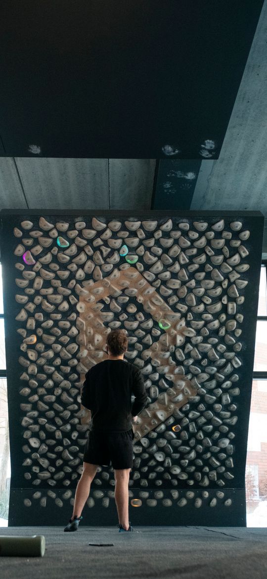 A climber standing in front of a training board, reading the problem