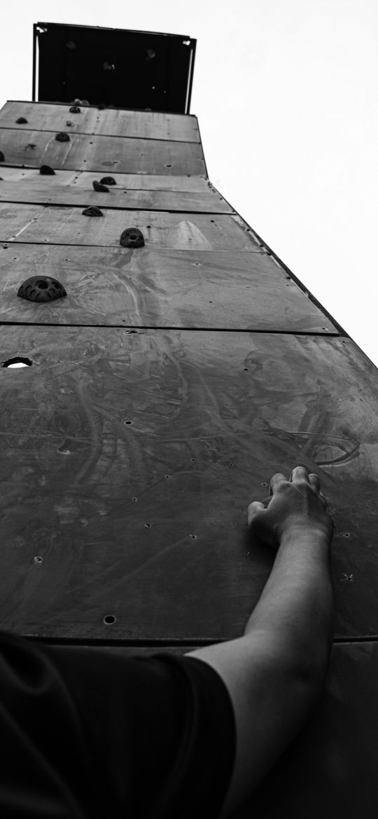 A hand reaching for a hold on a tall dark climbing wall